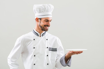 Smiling chef is holding plate on gray background.