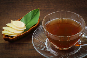 Ginger juice and fresh ginger with green leaves over wood
