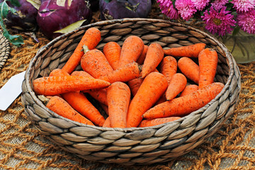 Fresh carrots in a wicker basket on the burlap background