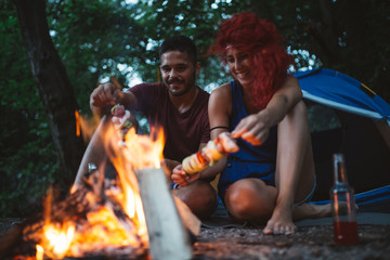Obraz na płótnie Canvas Happy young couple camping and hiking on wild mountain river. They sitting around campfire and making barbecue.
