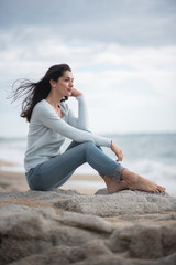 Fototapeta na wymiar A beautiful young brunette sitting on a rock at the beach