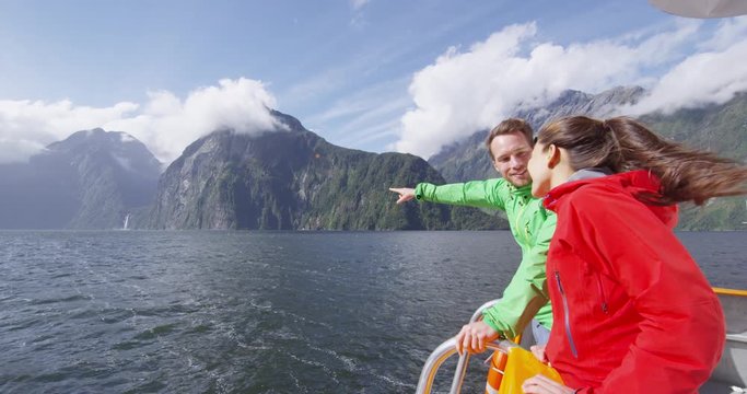 New Zealand Cruise ship tourists on boat tour in Milford Sound, Fiordland National Park, New Zealand. Happy couple on sightseeing travel on New Zealand South Island. Man pointing at waterfall.