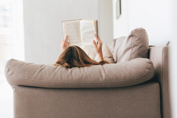 Back view of woman lying and reading book