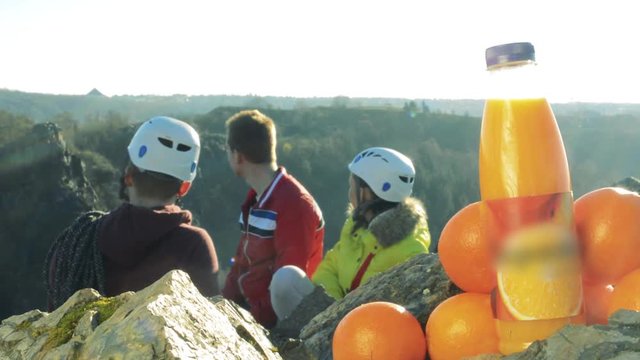 Three rock climbers look at the horizon - a bottle of juice in a pile of oranges in the foreground