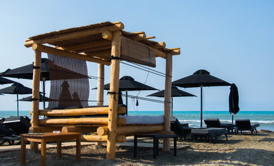 beutiful beach with  wooden big sun bed and black  and white beach umbrellas and sun beds against turquise see and blue sky 