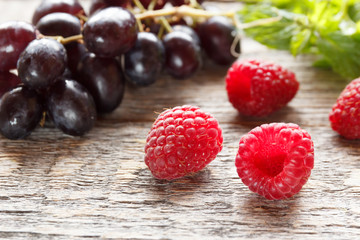 Berries of ripe raspberry and black grapes on a wooden background. Selective focus.