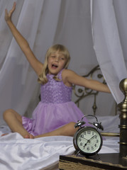 Alarm clock standing on bedside table. Wake up of an asleep young girl is stretching in bed in background