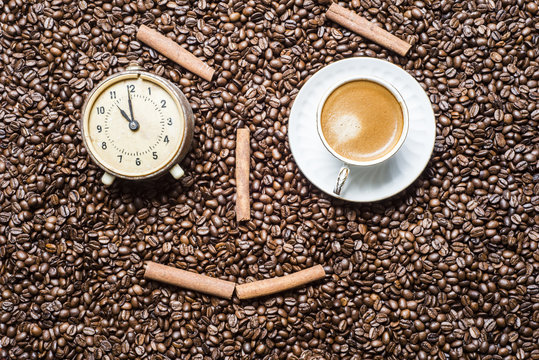 A cup of coffee and an alarm clock on the background of coffee beans