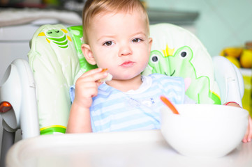 little kid chews a piece of muffin while sitting in his high chair
