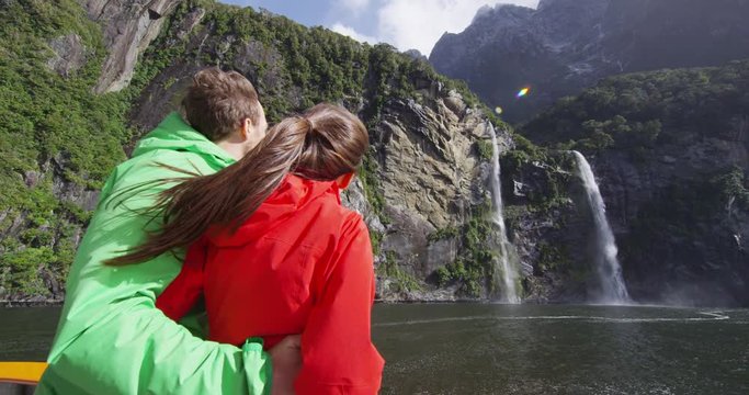 Cruise ship tourists on boat tour in Milford Sound, Fiordland National Park, New Zealand. Happy couple on sightseeing travel sailing by fairy falls waterfall on New Zealand South Island. SLOW MOTION.