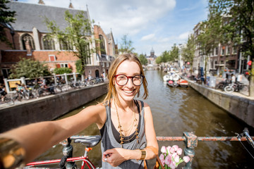 Naklejka premium Young woman tourist making selfie photo standing on the bridge in Amsterdam old city