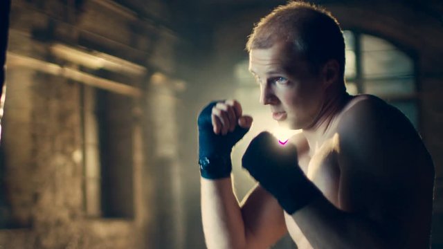 Muscular Shirtless Man Hits Punching Bag with His Fists. Part of His Gym Training. Shot on RED EPIC-W 8K Helium Cinema Camera.
