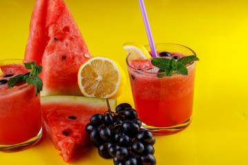Watermelon smothie and slices with lemon on yellow background
