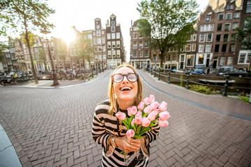 Portrait of a young and happy woman holding a bouquet of pink tulips standing outdoors in Amstredam city