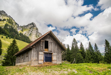 Wooden house or barn near the hiking trail in Switzerland, swiss Alps, forest, green grass.