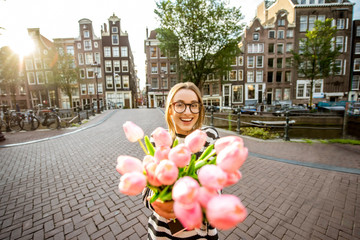Fototapeta premium Portret młodej i szczęśliwej kobiety z bukietem różowych tulipanów stojących na zewnątrz w mieście Amstredam
