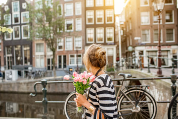 Naklejka premium Styl życia portret kobiety idącej z bukietem różowych tulipanów w pobliżu kanału wodnego w mieście Amsterdam