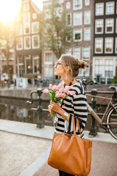 Lifestyle portrait of a woman walking with bouquet of pink tulips near the water channel in Amsterdam city