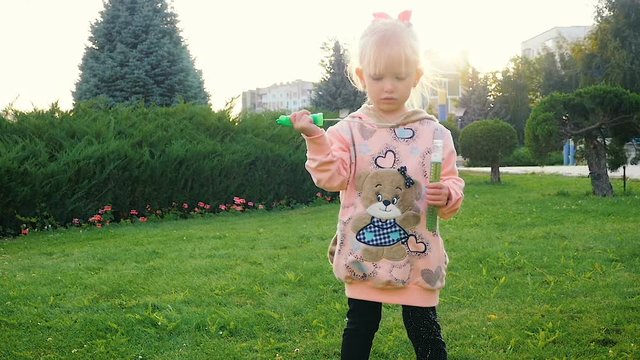 SLOW MOTION: little funny girl of two-years blowing soap-bubble in the city park.