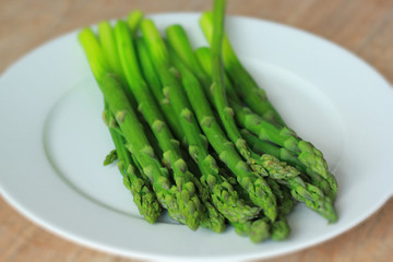 Boiled bunch of green asparagus on white plate on the wooden table