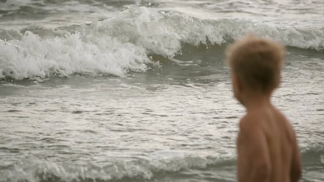 Little boy wondering sea waves on water surface, slowmotion shot at 120FPS