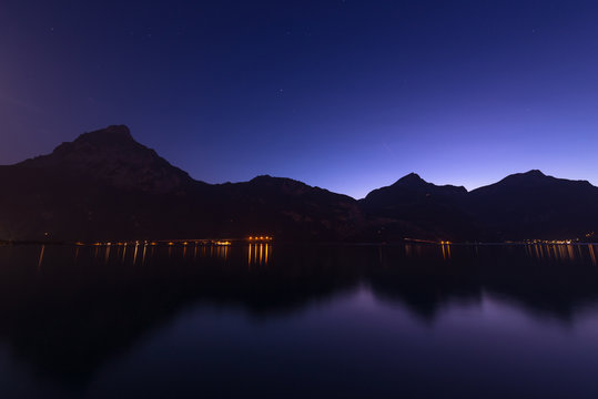 Lake. Night. Night panorama. Mountains, lake, reflection of lights in the water. Switzerland. Canton of Uri.