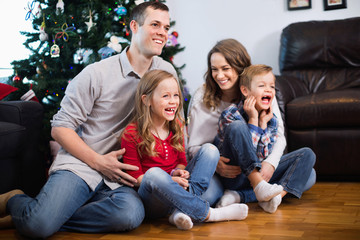 Young happy family sitting by Christmas tree at home