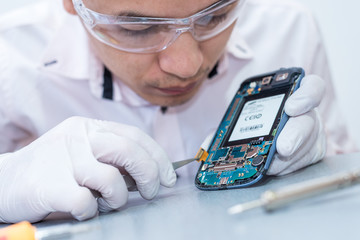 The asian technician repairing the smartphone's motherboard by soldering in the lab. the concept of...