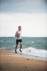 Gray haired man in sportswear runs on the beach