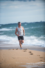 Fototapeta na wymiar Gray haired man in sportswear runs on the beach