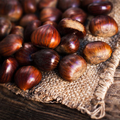 Ripe chestnuts on old wooden table and sack napkin close up with copy space. Roasted Chestnuts for Christmas.
