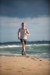 Gray haired man in sportswear runs on the beach