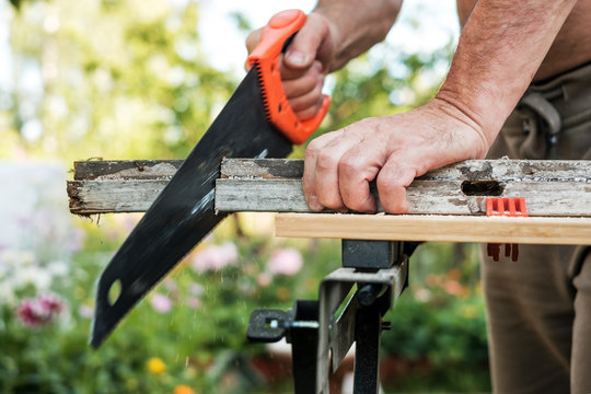 Caucasian man working cutting plank with handsaw outdoor in summer.