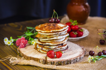 Homemade ruddy pancake with strawberry and cherry on a wooden stand