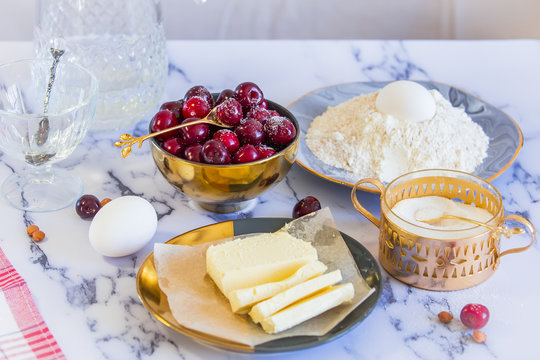 Ingredients for the pie - cherry, flour, eggs, sugar, water and butter on a white marble tabletop