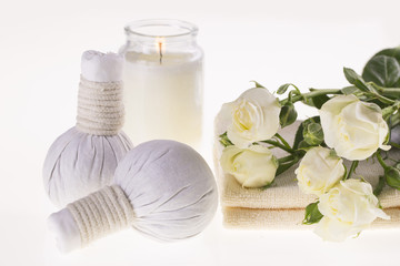 Fototapeta na wymiar Spa. Burning candle, herbal balls for massage, white roses and a towel on a white background