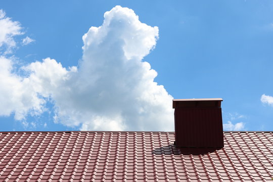 Red metal house roof tiles with brick roof chimney against blue sky background
