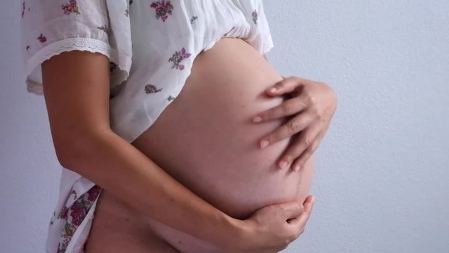 Image closeup of pregnant woman touching her belly with hands.