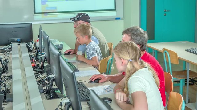 Kids are learning computer basics together with their grandparents in a computer lounge. 