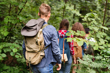 Naklejka na ściany i meble Teenagers with backpacks hiking in forest. Summer vacation.