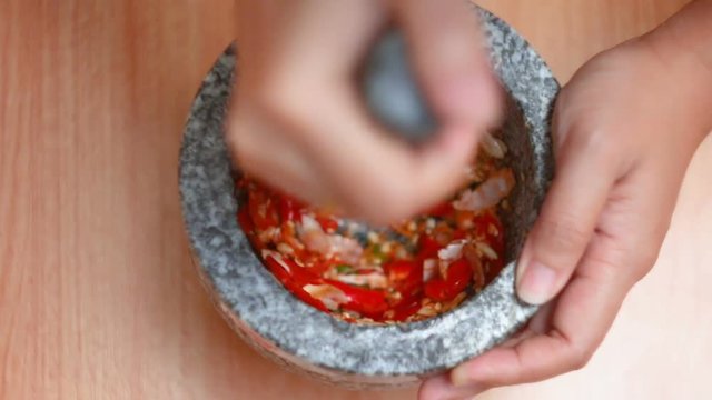 Top view hands of woman punching red hot fresh chilli and garlic with mortar stone prepare mixing herb seasoning before cooking thai food warm tone processed
