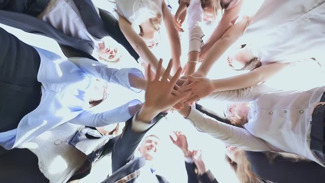 College Students Teamwork Stacking Hand Concept. Friendly graduates of the senior school put their hands on each other and open them against the white sky. Sunny daylight.