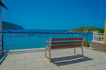 Beautiful sunny day in Sant Elm, with a public chair to enjoy the view in Majorca, with people enjoying the water, in Spain