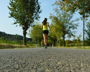 Fitness woman running on asphalt road. Long view.