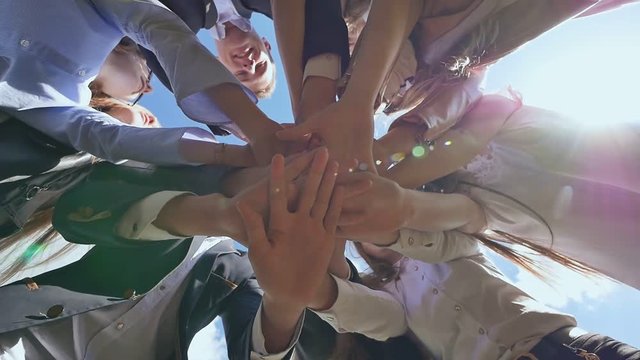 Friendly graduates of the senior school put their hands on each other and open them against the blue sky. Sunny daylight. College Students Teamwork Stacking Hand Concept.