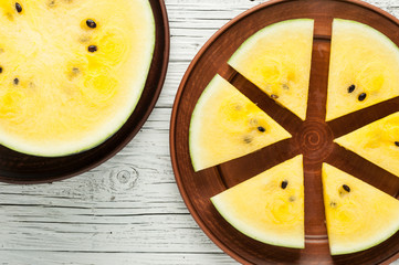 yellow watermelon slices on plate on white wooden background top view