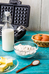 Making waffles at home - waffle iron and ingredients - milk, eggs and flour.