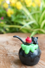 Halloween black cat. Miniature of Halloween black cat is making magic potion with poison red apple on top. Abstract background of flower garden with natural light. Soft focus on the cat's face