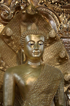 Antique gold Buddha statue covered in golden robes at temple in Myanmar.