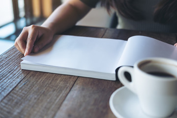 Closeup image of a woman reading and opening a white blank book with a white coffee cup on wooden table in vintage cafe
